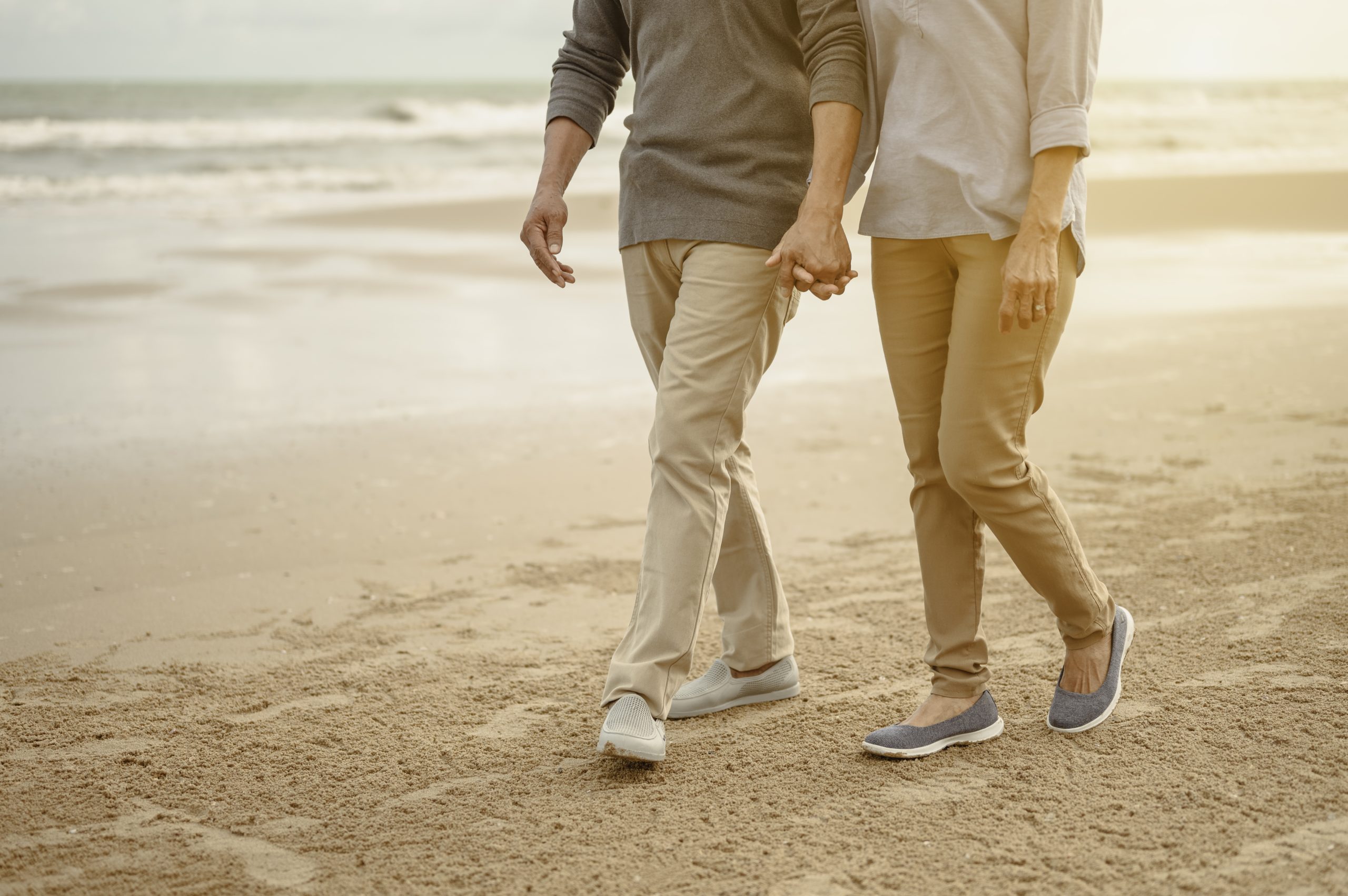 Senior lovers walk hand in hand at the beach at sunset, plan life insurance at retirement concept.