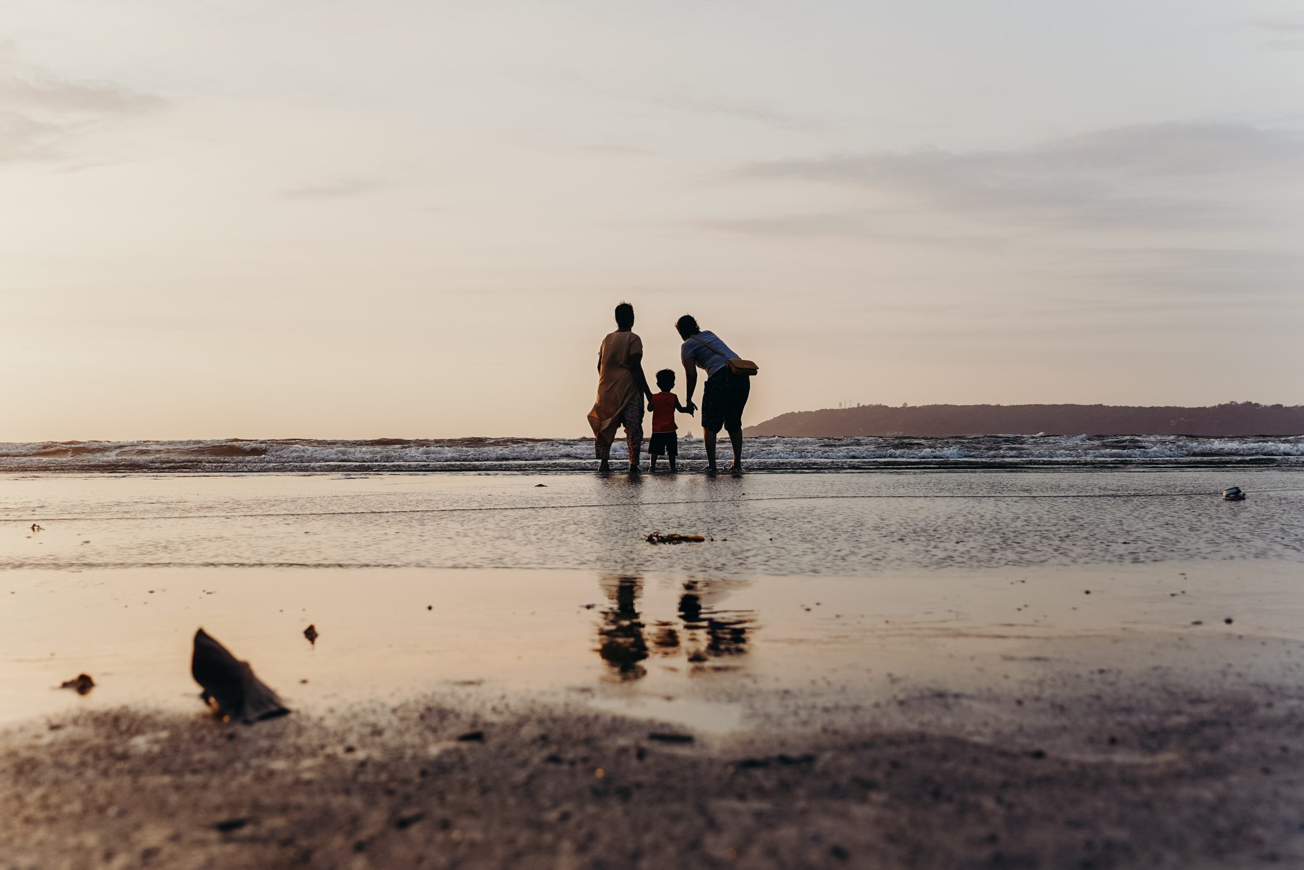 Family of three walking on the beach. Wet sand with a low hill also visible.