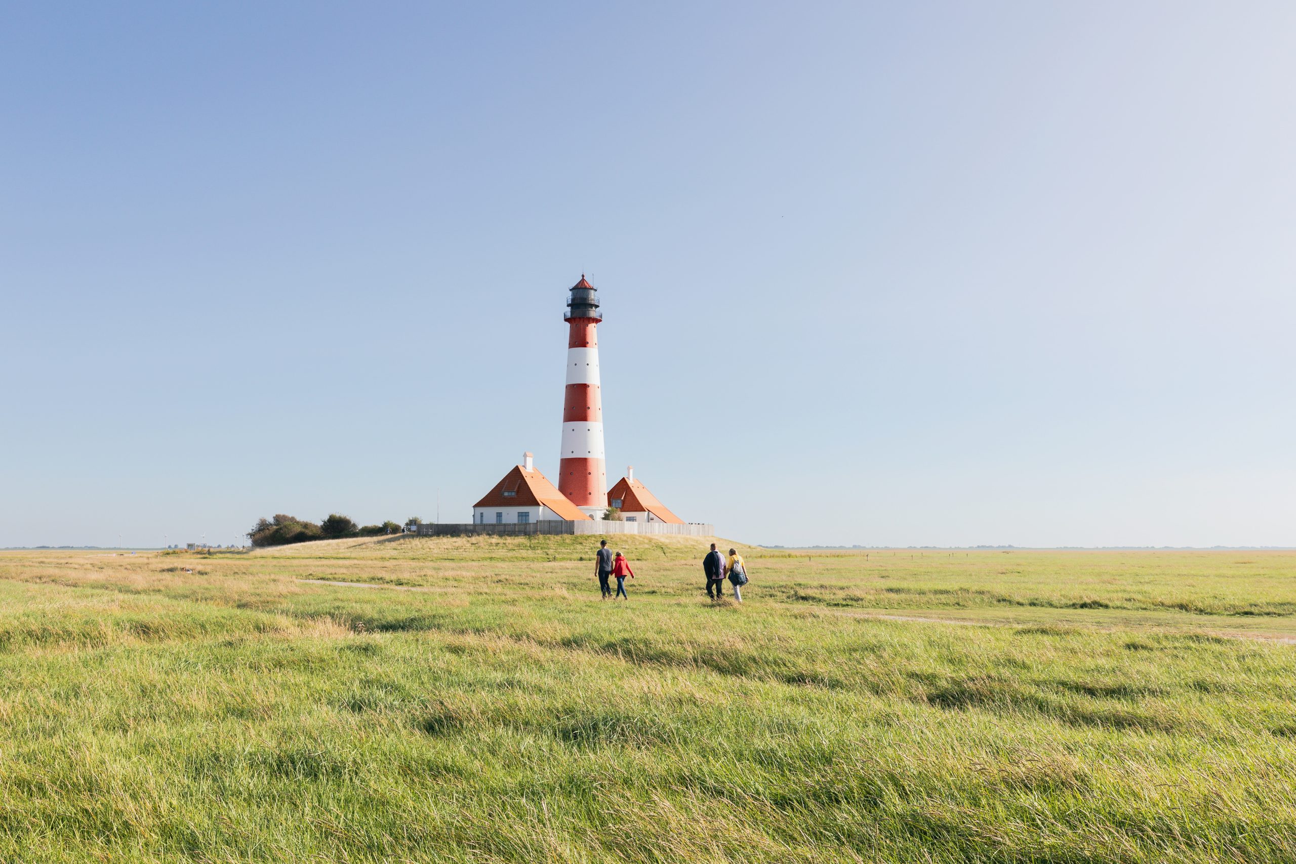 Family walking through a field. Shelter with an attached lighthouse in the distance.