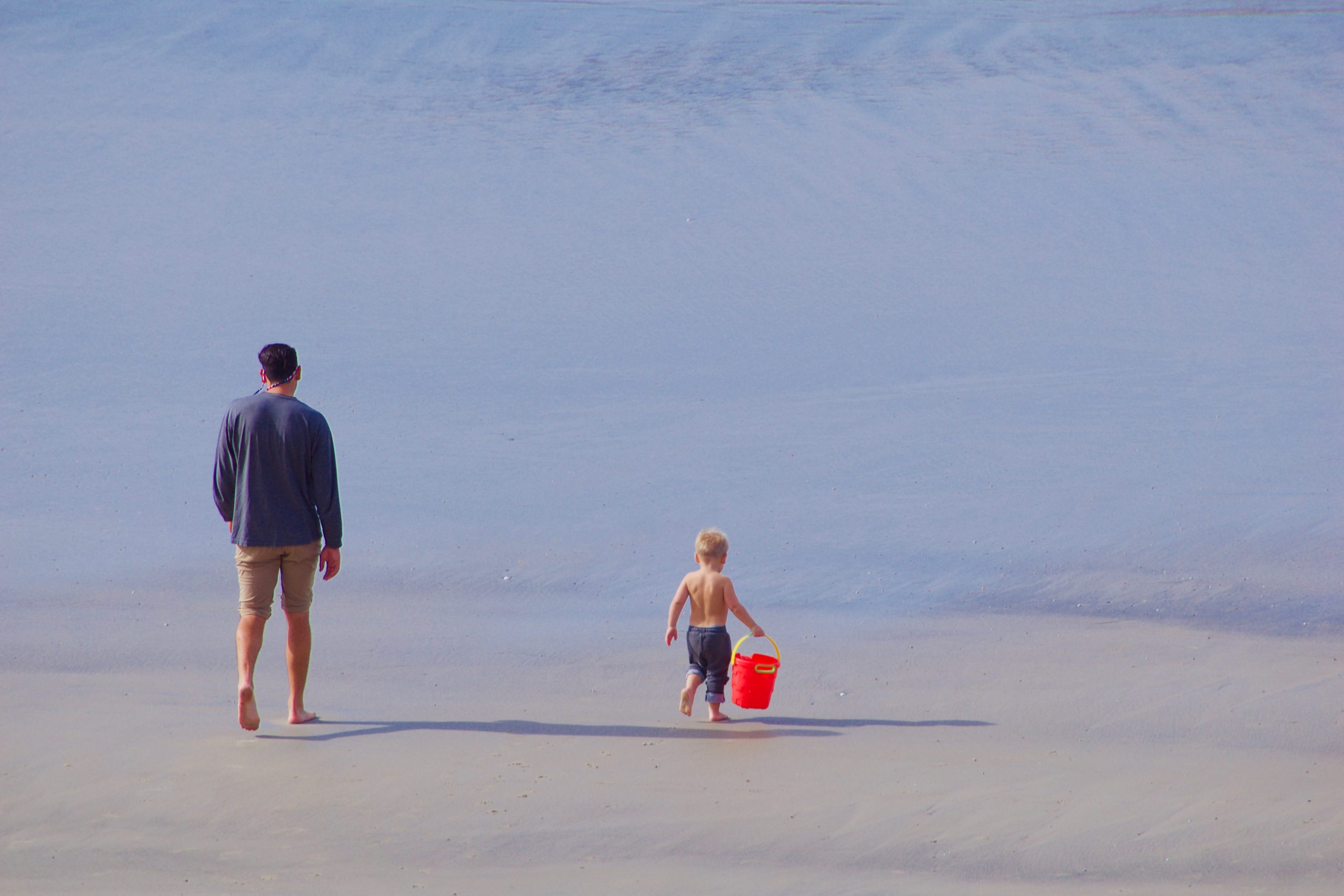 A father and his son walking on the sand at the beach