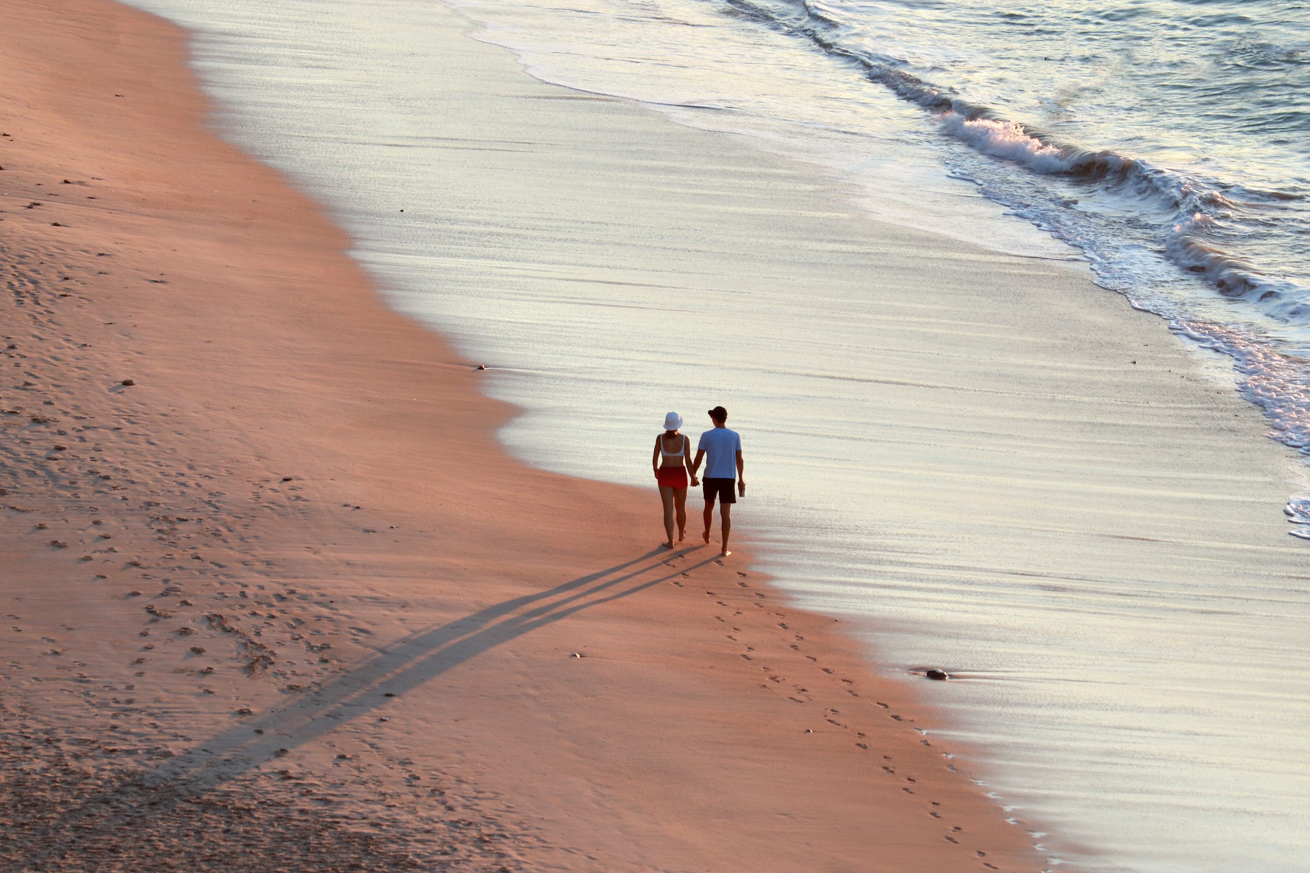 couple walking hand in hand on the beach by the sea