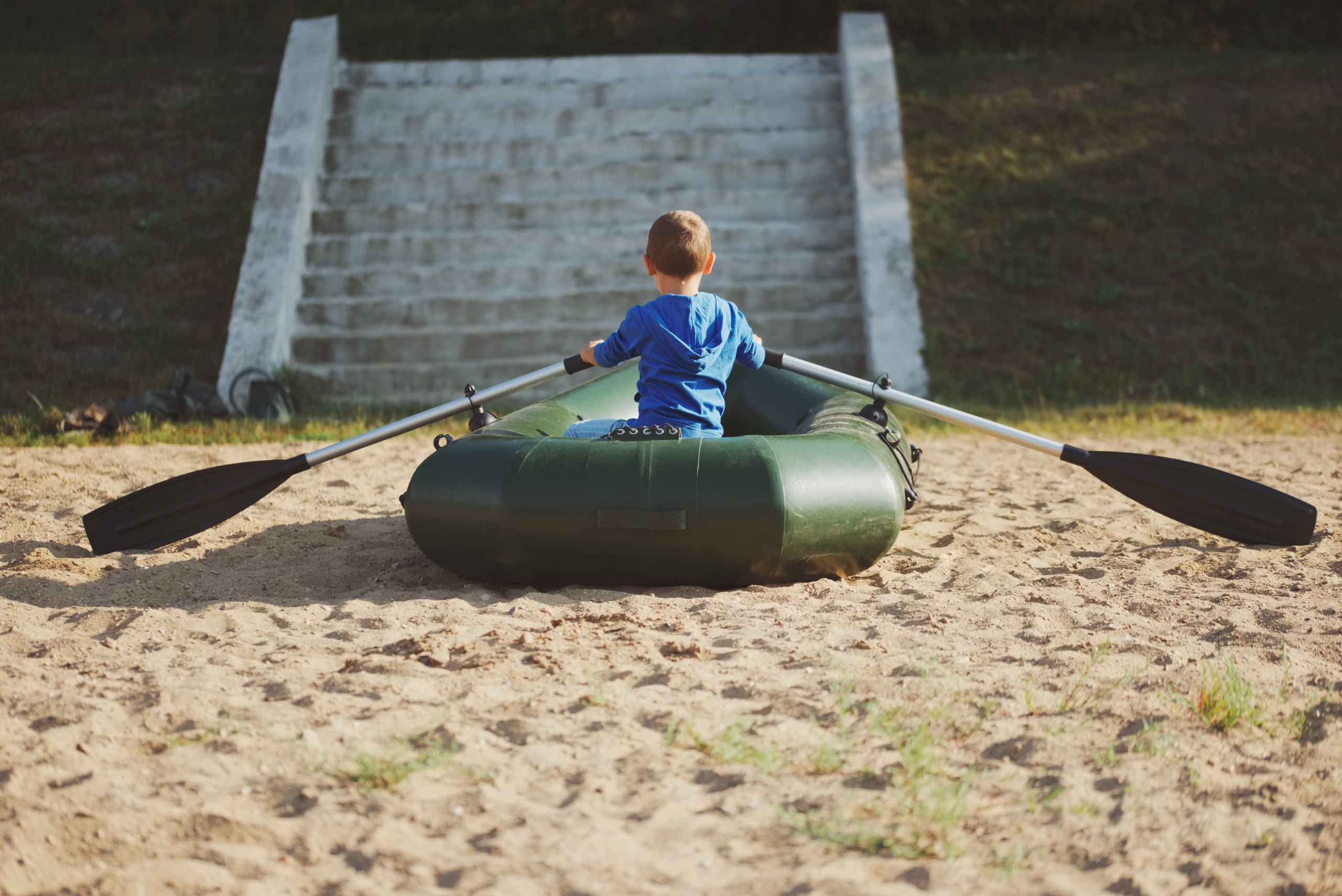 little boy swimming in inflatable boat on sandy beach