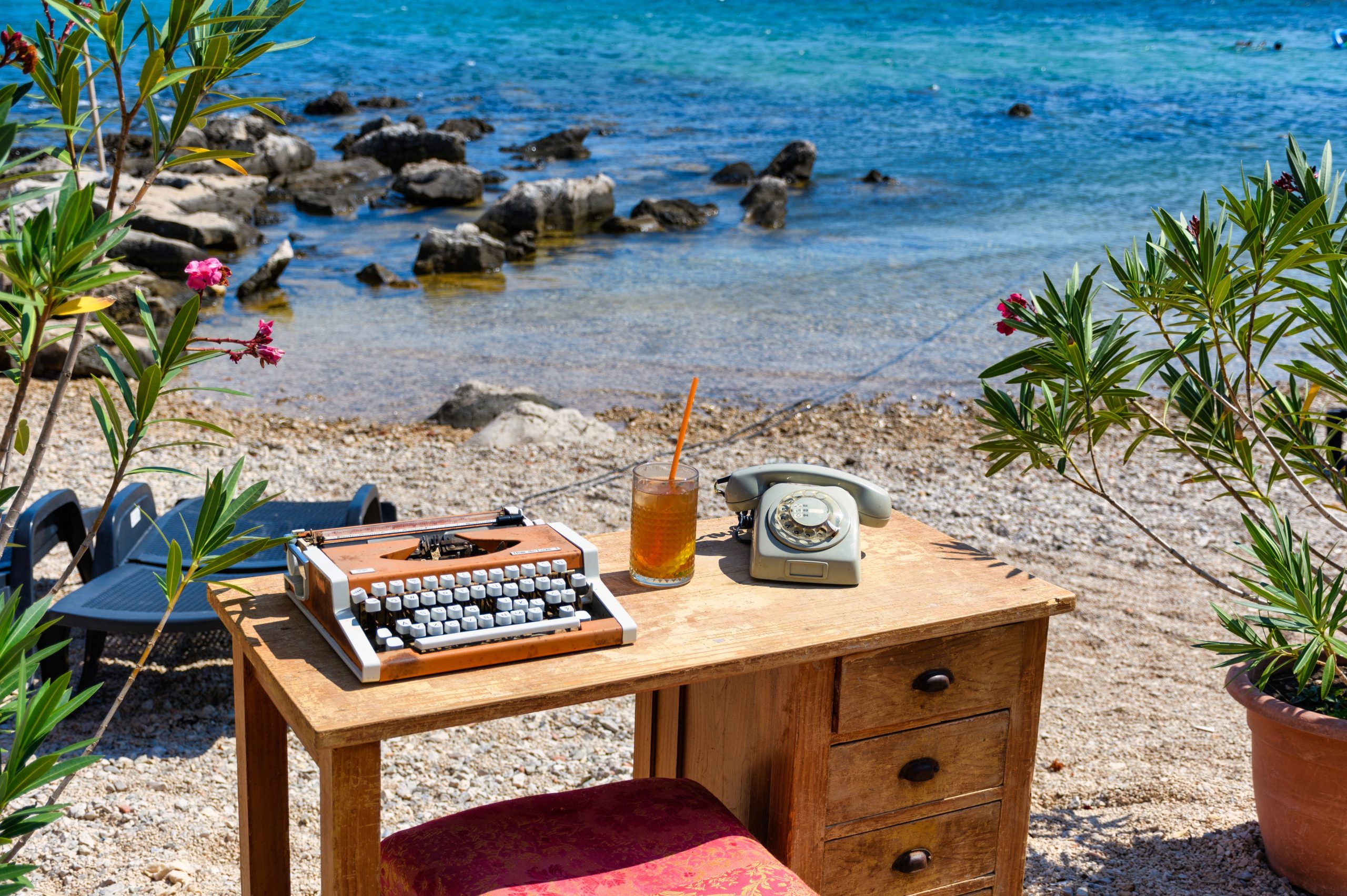 Vintage desk with a typewriter and an old phone. Glass of ice cold ice tea on old wooden table on beach.